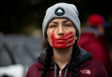 indigenous woman with red painted hand over mouth