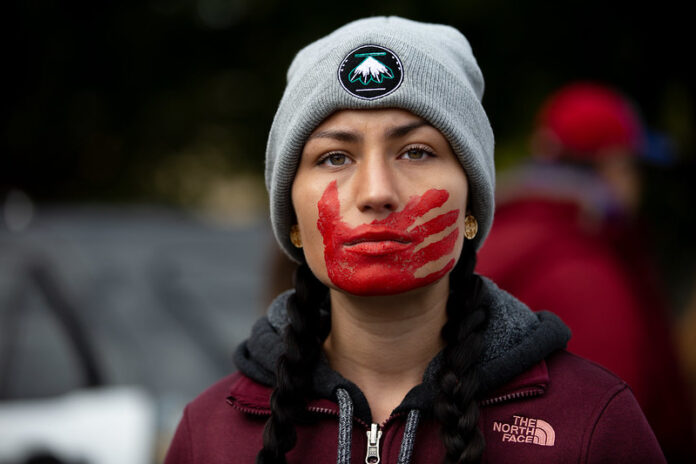 indigenous woman with red painted hand over mouth