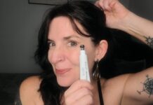 Annette Benedetti holding a tube of august + monroe brightening eye serum up to her cheak
