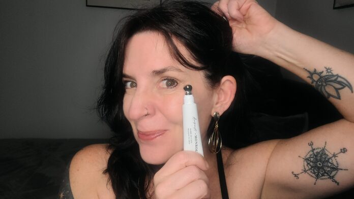 Annette Benedetti holding a tube of august + monroe brightening eye serum up to her cheak